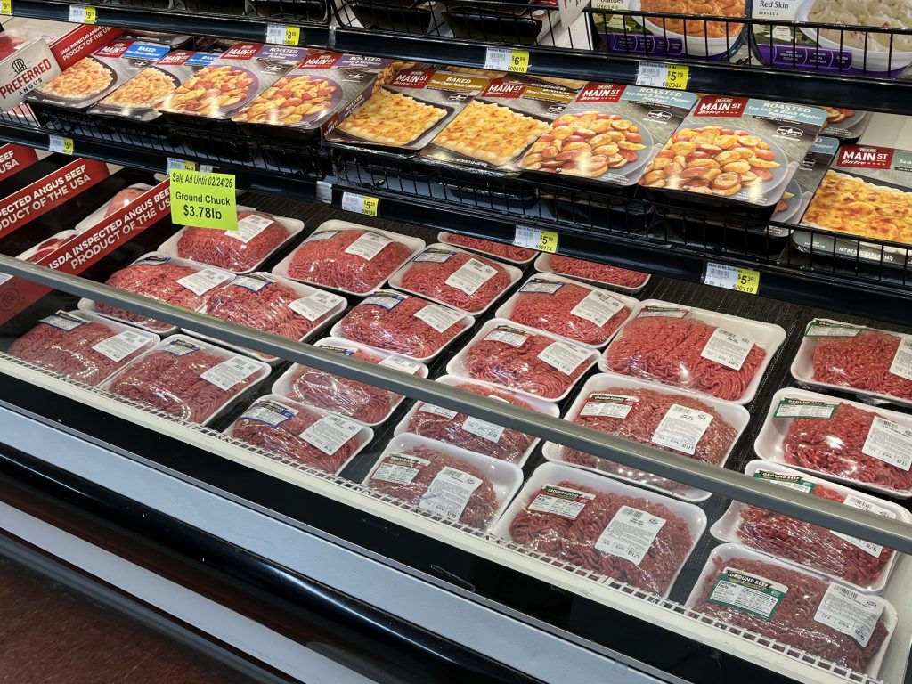 Packages of ground beef and other items in an open cooler in a grocery store.